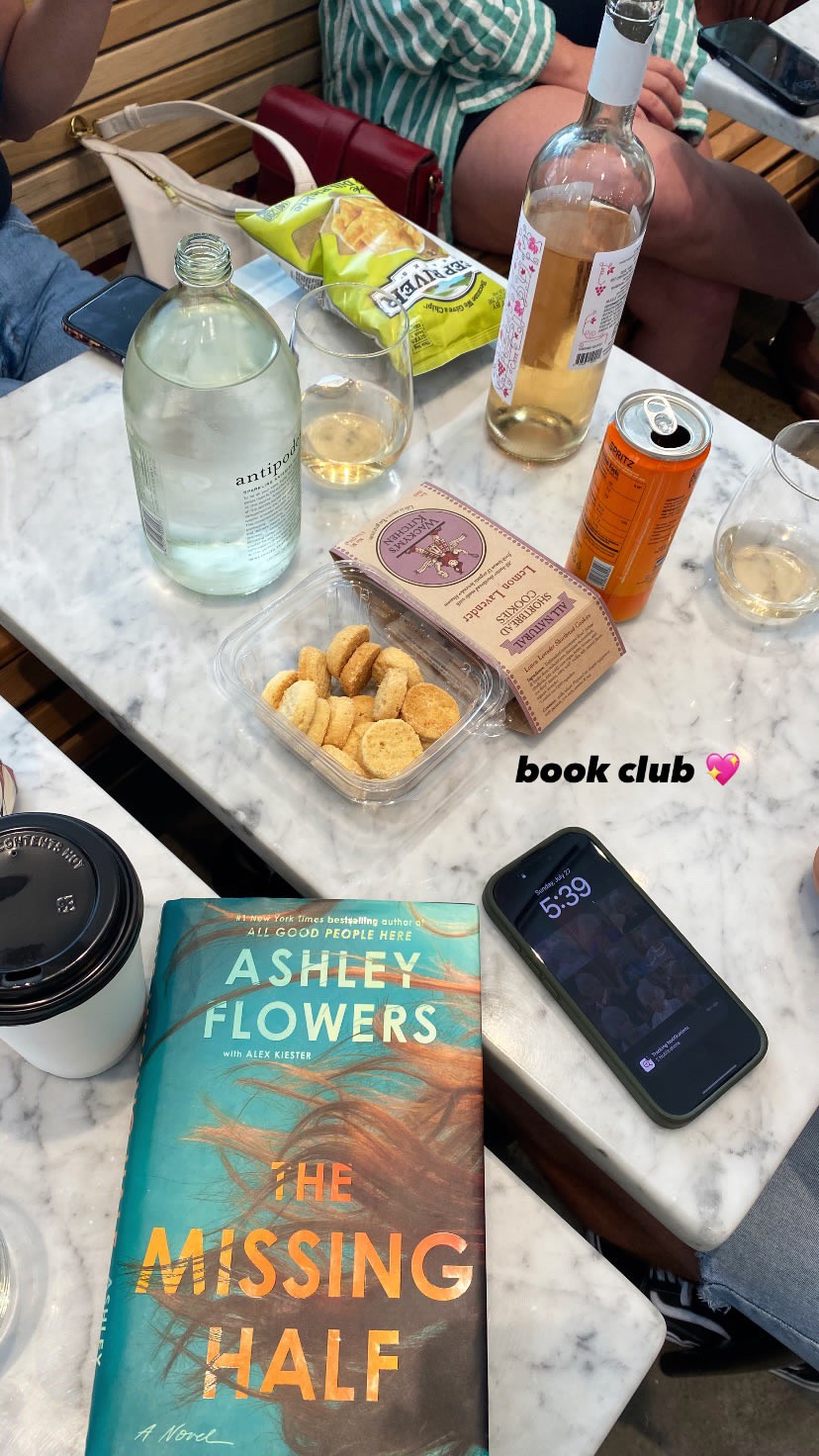 Book club gathering at Ari’s Pantry Downtown Dallas with wine, snacks, and The Missing Half by Ashley Flowers on the table